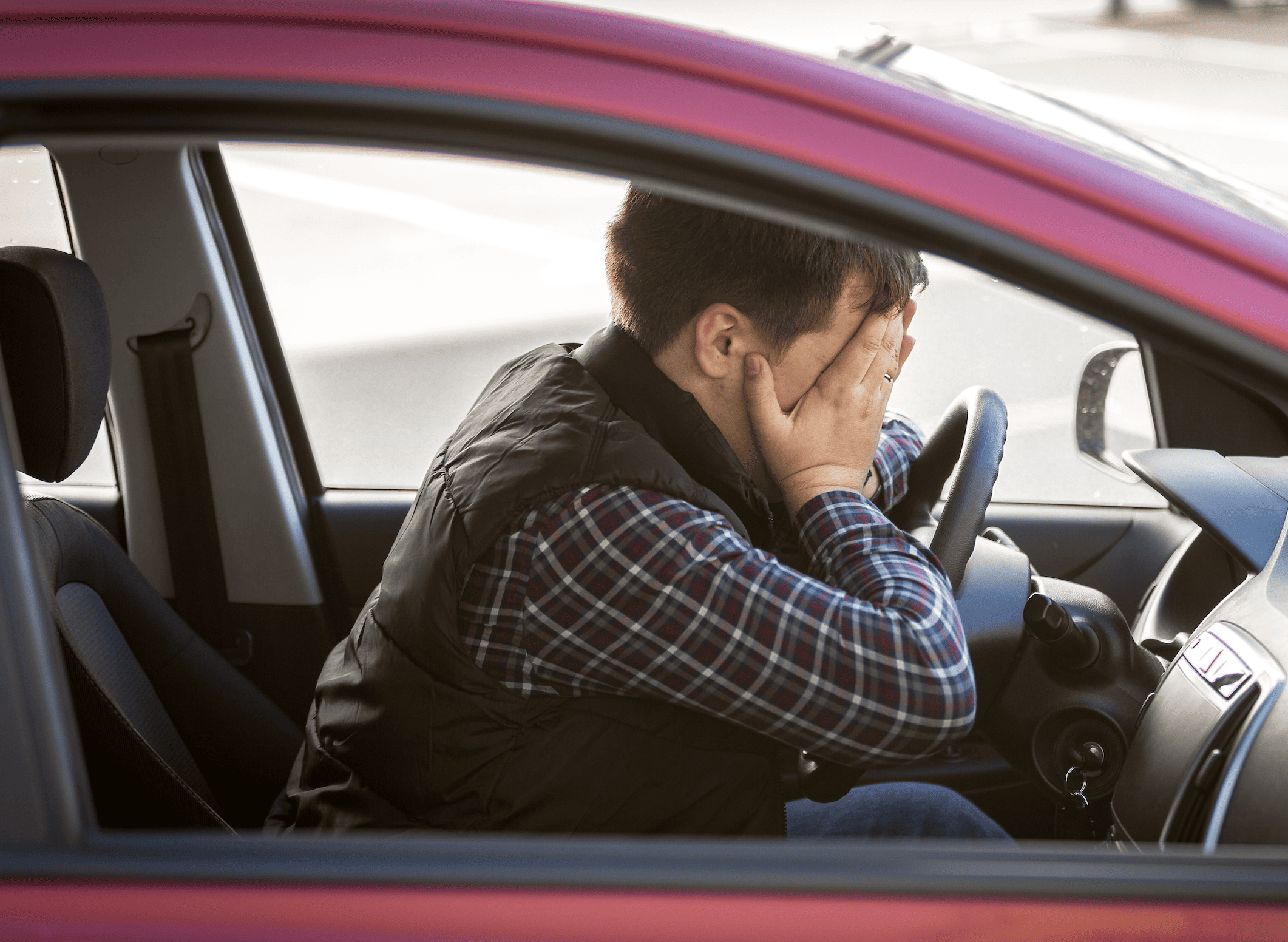Homme dans une voiture rouge se prenant la tête dans les mains par angoisse